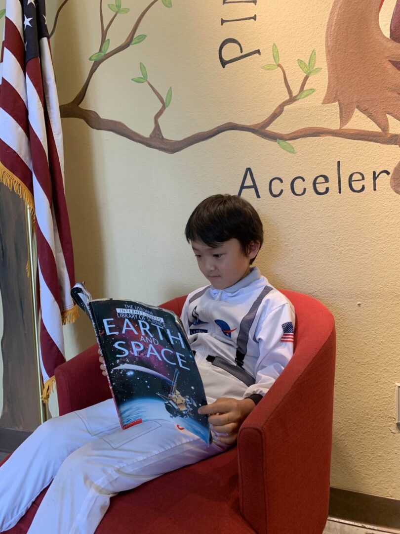 A boy sitting in a chair reading an earth space book.