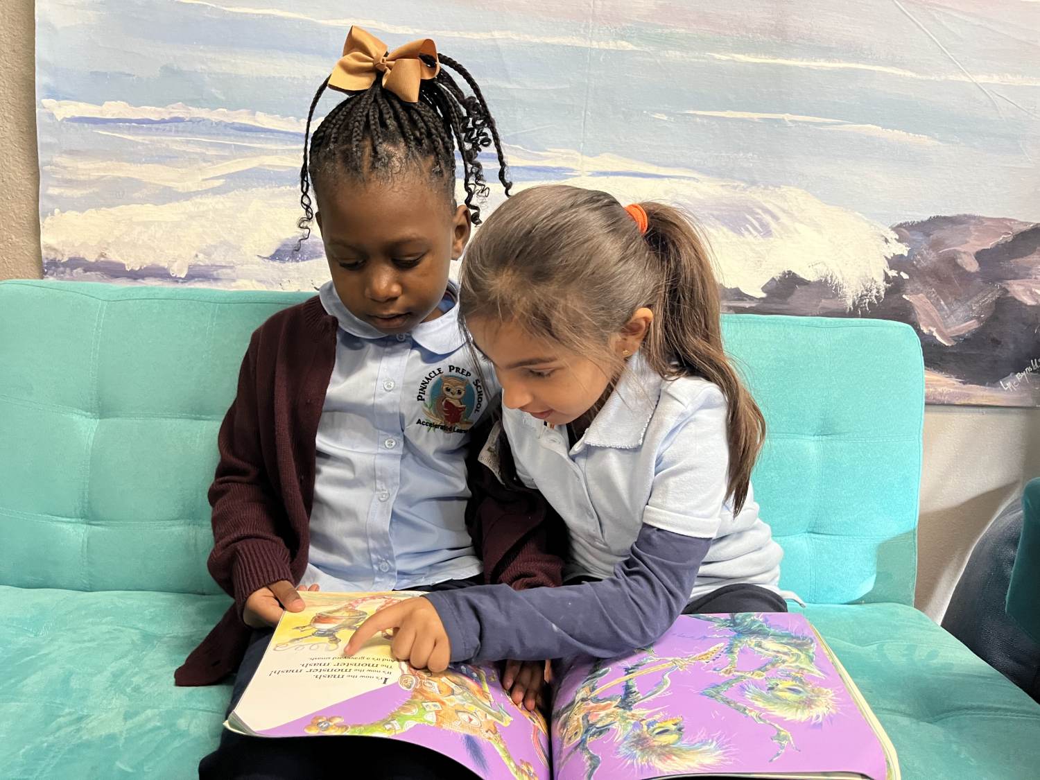 Two children sitting on a couch looking at an open book.